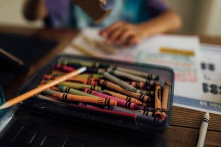 Canva – Tray of crayons with kid in the background